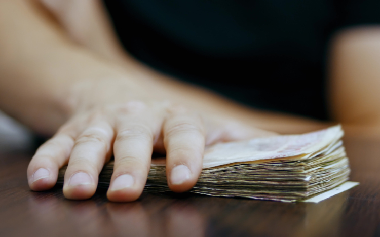 A hand on top of a pile of banknotes